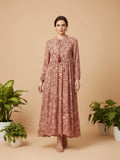 Woman wearing a floral dress standing against a beige background with plants around.