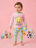 Child wearing a Looney Tunes-themed pajama set with a pink shirt and blue pants, standing against a pink background.