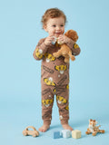 Child wearing a brown pajama set with cartoon characters, holding a teddy bear on a blue background.